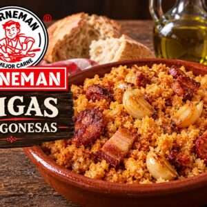 Un plato de migas aragonesas presentadas junto a trozos de pan, una aceitera y una cabeza de ajos